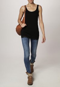 Zwarte tanktop met kanten rand, blauwe skinny jeans en tan enkellaarsjes; model met een bruine schoudertas.