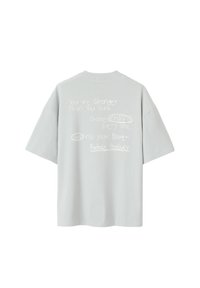 T-shirt oversize gris clair avec du texte motivant imprimé en blanc dans des styles variés au dos. Manches courtes et col rond.