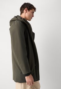 Olijf groen waterdichte jas met een capuchon, voorzien van een gladde textuur, aan de voorkant sluitend met drukknopen en contrasterende zwarte manchetten.
