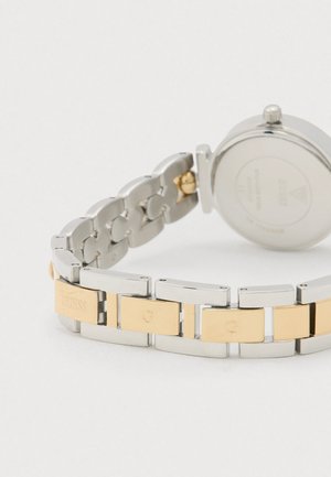 Ezüst és arany fém óraszíj arany színű hivatkozásokon gravírozott "GUESS" és "G" felirattal, hátulnézetből.