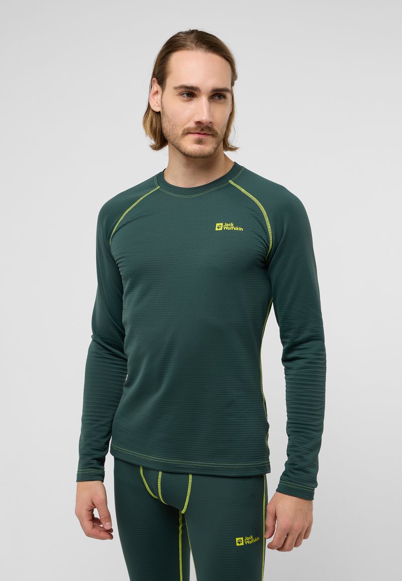 Haut thermique à manches longues en vert foncé avec un tissu texturé, rehaussé de surpiqûres jaunes vives et d'un logo. Design ajusté pour le superposition.