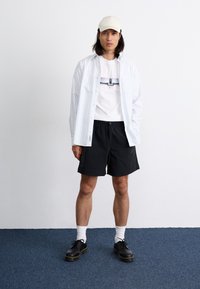 Hvit og blåstripet skjorte med knapper over en grafisk hvit t-skjorte, svarte shorts, hvite sokker og svarte sko. Lyse farget caps.
