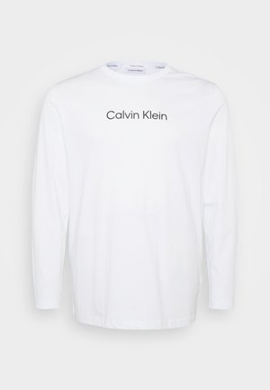 Dlhý rukáv biele tričko vyrobené z bavlny, ktoré má okrúhly výstrih a logo "Calvin Klein" potlačené tmavosivou farbou cez hrudník.