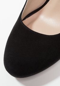 Černé semišové lodičky na vysokém podpatku s kulatou špičkou, otevřenými stranami a hladkým vnitřním povrchem. Jemné prošíván�í podél okrajů.