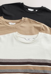 Tre magliette nere, beige e bianche, con scollature rotonde e texture diverse. La maglietta bianca presenta motivi a righe in tonalità terrose.