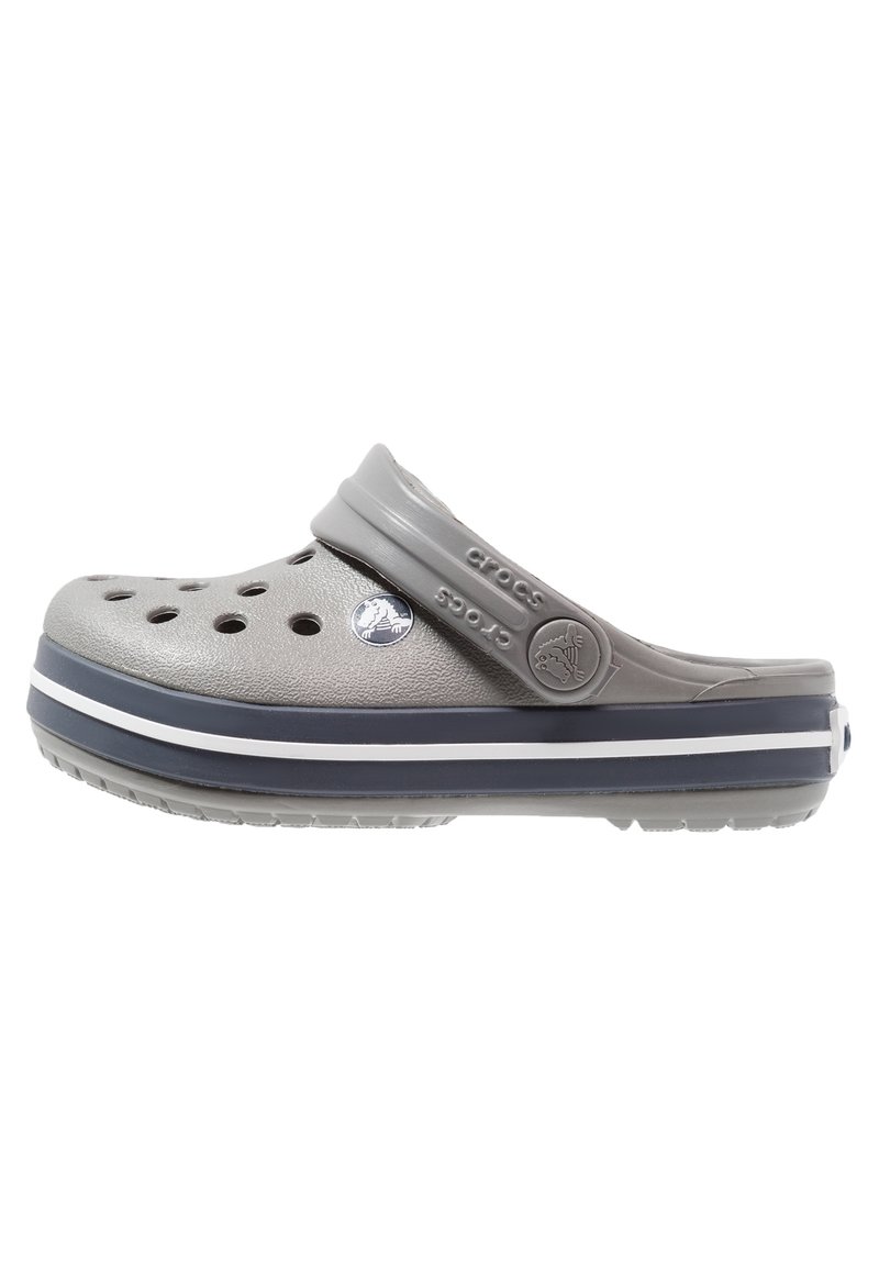 Sabot Crocs gris avec trous de ventilation, bride réglable au talon et semelle épaisse bleu marine avec des rayures blanches.