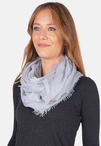 Écharpe gris clair en tissu doux et texturé, avec des bords effilochés, enroulée lâchement autour du cou.