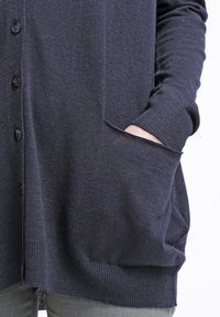 Marinblå cardigan i texturerad stickad tyg, med knappar, två framfickor och ribbade muddar och nederkant. Minimalistisk design.