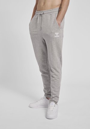 Grijze fleece trainingsbroek met een elastische tailleband en een trekkoord. Beschikt over zijzakken en een wit logo op de linkerdij. G draagt het met witte sneakers.