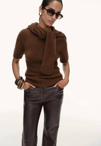 Brown knitted sweater with short sleeves and a scarf detail, paired with dark brown leather pants. Accessories include gold bangles.