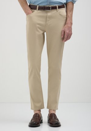 Pantaloni beige in misto cotone, slim fit, con passanti per cintura, tasche frontali e una texture liscia, abbinati a mocassini marroni.