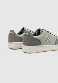 Zapatillas verdes y grises con un upper de cuero suave, talón texturizado, logo blanco en la parte trasera y cordones azul marino, con un diseño de caña baja.