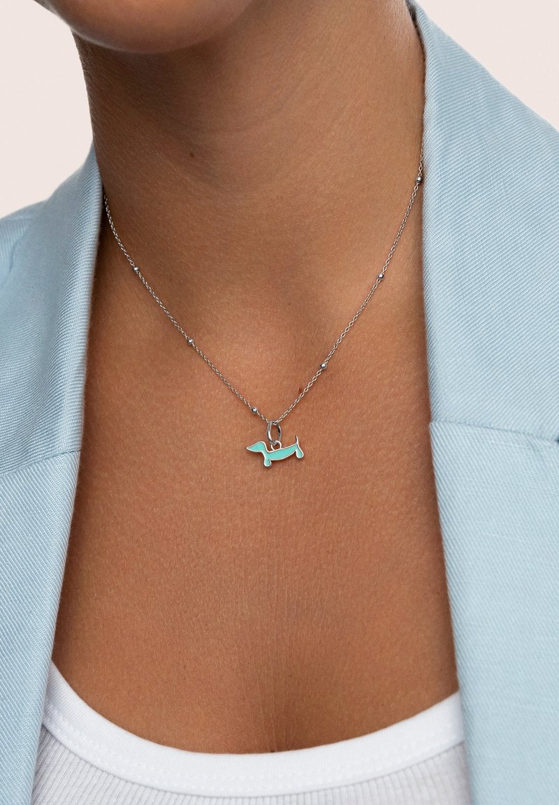 La collana in argento presenta un pendente a forma di bassotto smaltato in turchese, evidenziando il suo design giocoso e le sue superfici lisce a contatto con la pelle nuda.
