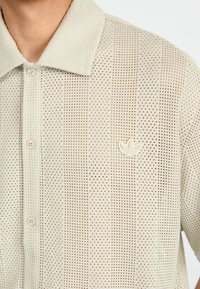 Light beige polo shirt featuring a textured, perforated design, quarter-button placket, and a small white logo on the left chest.