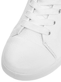 Biały skórzany sneaker o fakturowanej powierzchni z białymi płaskimi sznurowadłami zawiązanymi w krzyżak na przedniej górnej części.