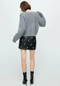 Suéter gris de punto corto con hombros caídos, combinado con una falda de cuero negra con tachuelas plateadas en un patrón disperso.