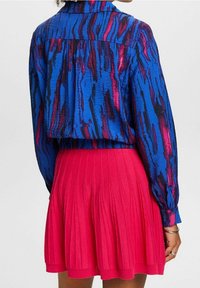 Haut bleu vif à manches longues avec un motif à rayures texturé en rose et noir, assorti à une jupe plissée rose unie.