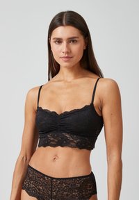 Bralette en dentelle noire avec des bretelles fines ajustables, présentant un devant froncé et des bords festonnés, assorti à un bas en dentelle coordonné.