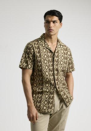 Camisa de manga corta en marrón con patrones geométricos y florales en crema. Tejido ligero, corte relajado y cuello puntiagudo. Pantalones en beige.