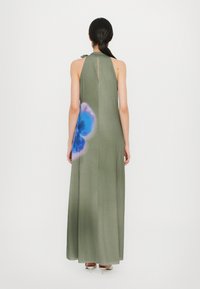 Olijfgroen halter maxi-jurk met een sleutelgatachterkant en een blauw bloemenpatroon aan de zijkant. Gemaakt van zachte, vloeiende stof met een gladde textuur.