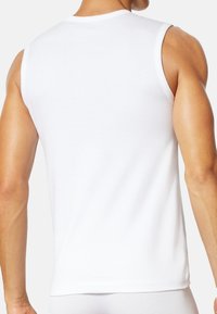 Débardeur en coton blanc sans manches, design ajusté, texture lisse, encolure ronde, et bras découverts mettant en valeur les contours musculaires.