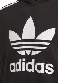 Černá mikina s kapucí, na které je velké bílé logo trefoil se třemi listy a třemi vodorovnými pruhy pod názvem značky "adidas."