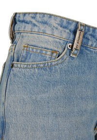 Hellblaues Denim-Jeans mit klassischem Fünf-Taschen-Design, sichtbarer Naht und einem Metallschild mit der Aufschrift "STUDIOS" in der Nähe des Taillenbunds.