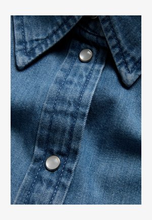 Denimskjorte i mellemblå, med spidse kraver, sølvfarvede trykknapper og subtil tekstur med kontraststingdetaljer.