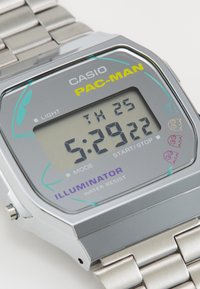 Montre numérique en argent avec un cadran rectangulaire arborant un fond gris, des accents jaunes et turquoise, des graphismes Pac-Man, et un bracelet métallique.