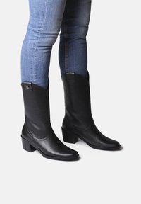Mustad mustad nahast cowboy saapad, millel on kerge konts, terav nina ja külgmised õmblused. Kandmise all on tihedad sinised teksad.