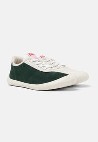 Baskets en daim vert avec une semelle en caoutchouc blanche et une marque rose sur la languette, angulées pour montrer le côté et l'avant.