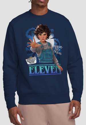 Navy sweatshirt showing Eleven from Stranger Things in overalls reaching forward, with "Friends Help Friends" and show logo text.