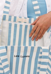 Gestreepte totebag van blauw en wit katoen. Bevat een klein zakje en een label met de tekst "Les Lunes" aan de voorkant. De handvatten zijn ook gestreept.