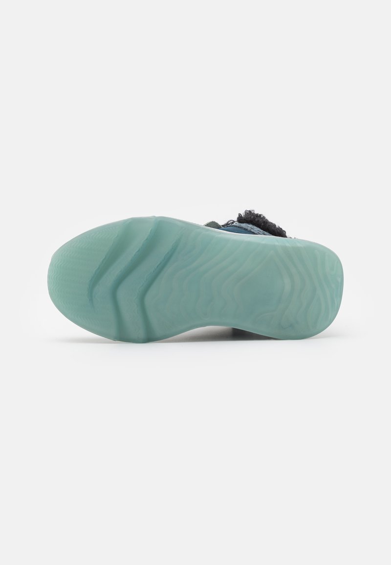 Schuhe mit einer durchsichtigen blauen Gummisohle, die eine wellenförmige Textur aufweist, ergänzt durch einen Oberteil in Schwarz und Blau.
