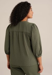 Blusa verde oliva con maniche a sbuffo, motivo testurizzato e dettaglio delle spalle arricciato. Tessuto morbido con una vestibilità comoda e orlo arrotondato.