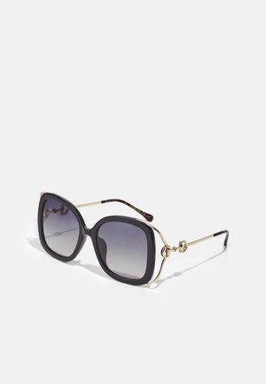 Óculos de sol oversized pretos com lentes graduadas, detalhes em metal dourado e um design de dobradiça único. O formato quadrado plano melhora a visibilidade.