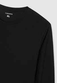 T-shirt nera a maniche lunghe in una morbida texture, con un design a girocollo e dettagli di cucitura sottili. L'etichetta riporta "TERRANOVA XL."