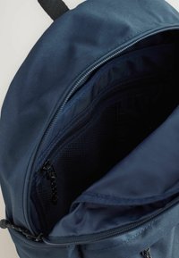 Zaino blu navy con apertura con cerniera, tasca interna in rete e tessuto liscio e resistente. Presenta un design semplice e strutturato.