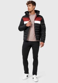 Jachetă neagră căptușită cu dungi orizontale roșii și albe, pantaloni skinny negri și adidași albi. Proiectată cu glugă și închidere cu fermoar.
