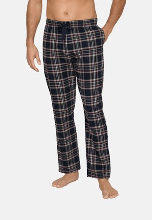 Mannelijk model dat marineblauwe en grijze geruite pyjamabroek met trekkoord draagt, staand op blote voeten met één hand in de zak tegen een witte achtergrond.