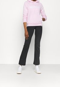Rosa Baumwoll-Hoodie mit weißem "adidas"-Logo und Vorderfach, kombiniert mit schwarzen, eng anliegenden Hosen und weißen Sportschuhen.