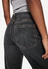 High-waisted black denim jeans with contrast stitching, featuring two back pockets and a relaxed fit. The fabric has a slightly textured finish.