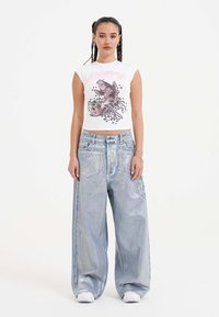 White short-sleeve crop top with a pink graphic design; paired with oversized light blue denim jeans featuring side pockets and a smooth texture.