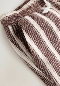 Pantalones de tela texturizada con rayas marrones y blancas, con cintura elástica y cordón blanco, doblados sobre una superficie neutra.