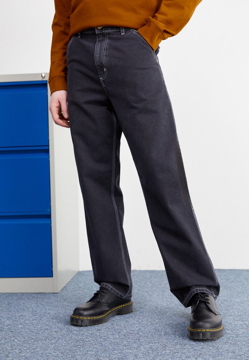 Mørke denimbukser med løs passform, som har kontrasterende hvite sømmer og sideakenter. Bært med svarte sko med gule detaljer.