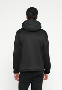 Svart hettejakke med en glatt, matt finish. Har polstret hette, elastiske mansjetter og en vanlig passform. Litt teksturert bakpanel.