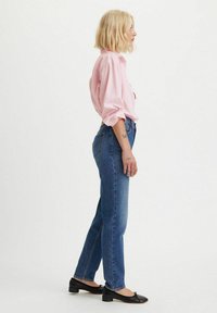 Camisa a rayas de color rosa claro, jeans de tiro alto azul y zapatos planos negros. El atuendo presenta un corte relajado y una textura clásica de mezclilla.