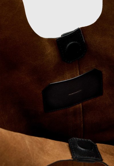 Gros plan d'un tissu en daim marron avec des patchs en cuir noir cousus sur la surface.