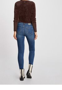 Strakke jeans van donkerblauwe denim, met een middelhoge taille, vijf zakken en een naaddetail aan de achterkant. Draag ze met contrasterende enkellaarzen.