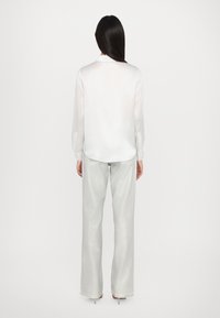 Witte, lange mouw, satijnen blouse met een gebogen zoom, gecombineerd met hoog-wijde, glanzende zilveren broek met brede pijpen, voorzien van een gladde textuur en minimale details.